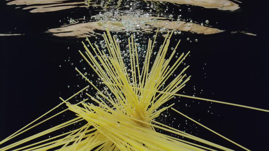 Raw spaghetti noodles are dropped into water