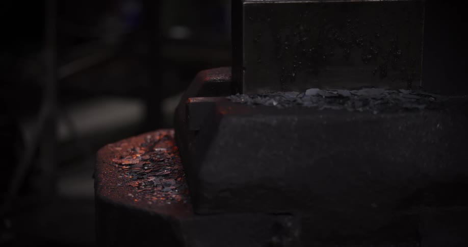 Macro shot of hot metal slag sizzling and steaming as water is sprayed onto it in a dark blacksmith shop