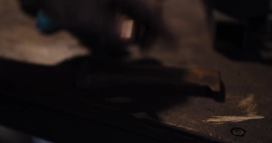 A close-up shot of a craftsman's hands wiping down a piece of metal on a workbench in a dimly lit workshop