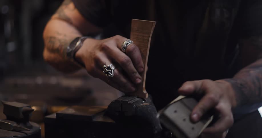 A tattooed artisan carefully sands a piece of wood held in a vise in his workshop