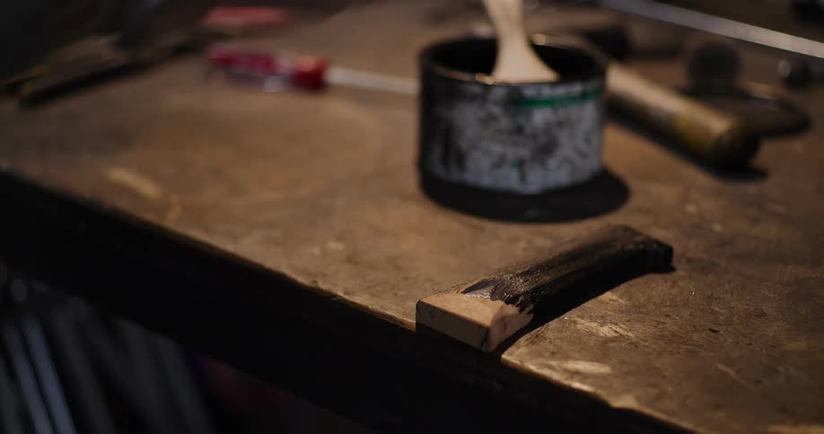 A tattooed craftsman carefully paints a wooden piece with black paint and wipes it down in their workshop