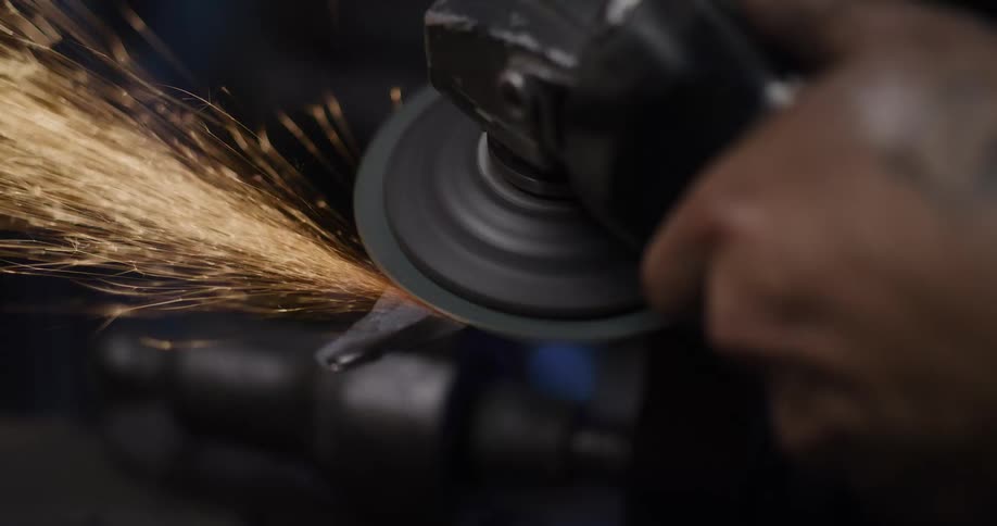 Slow motion close-up of a bladesmith shaping a metal blade with an angle grinder, creating a shower of brilliant sparks