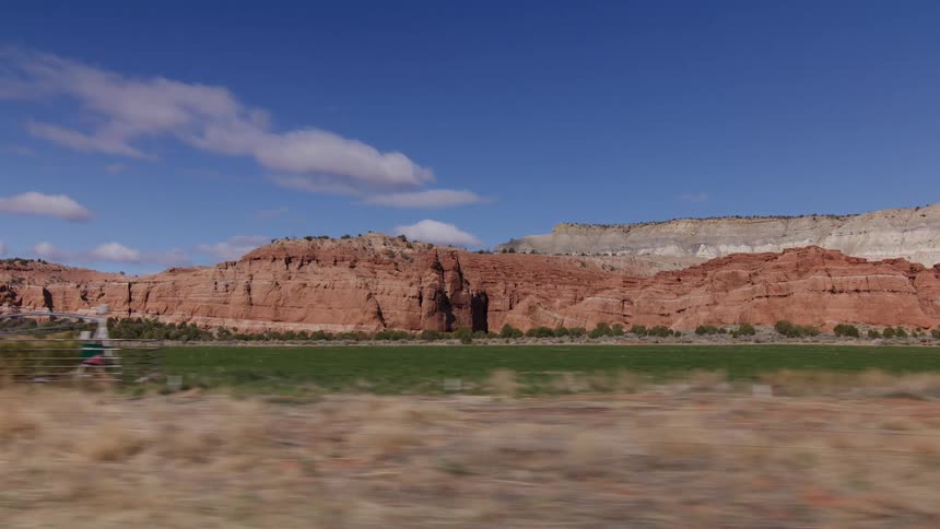 A slow-motion tracking shot reveals a lush green field and towering red rock formations under a bright blue sky in the American Southwest