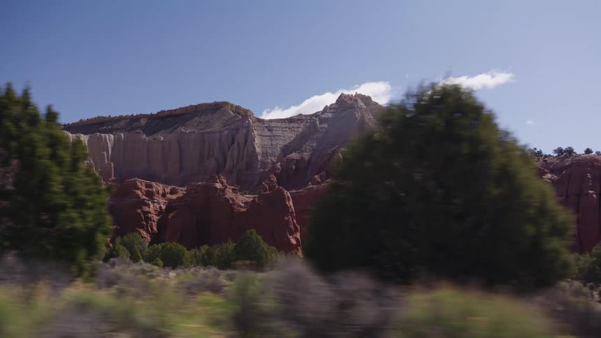 A slow-motion driving shot reveals the stunning red rock formations and colorful cliffs of a desert canyon