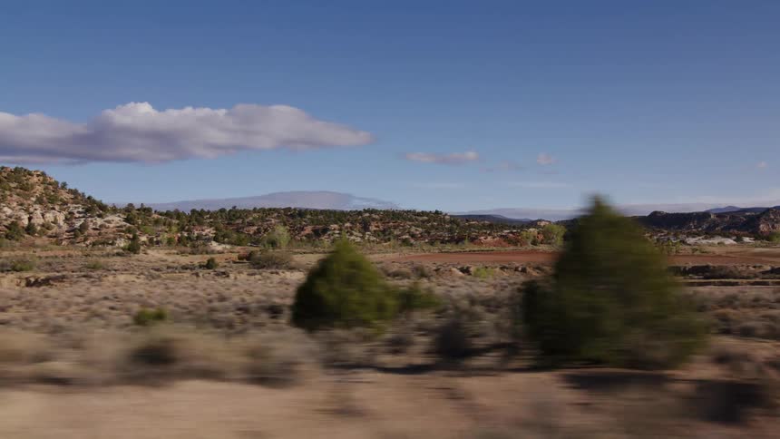 A scenic drive through a vast, arid valley reveals rocky hills and distant mountains under a clear blue sky