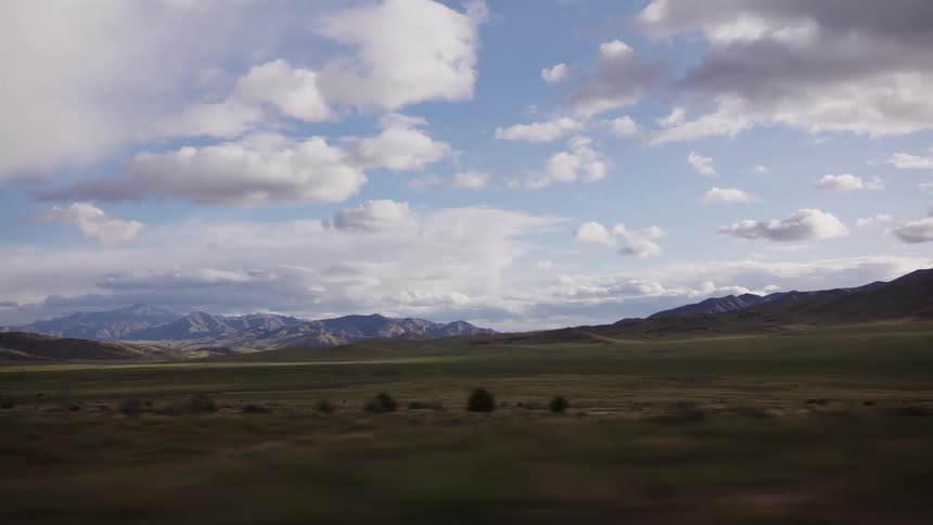 A scenic drive through a vast, open landscape with rolling green hills and distant mountains under a beautiful cloudy sky