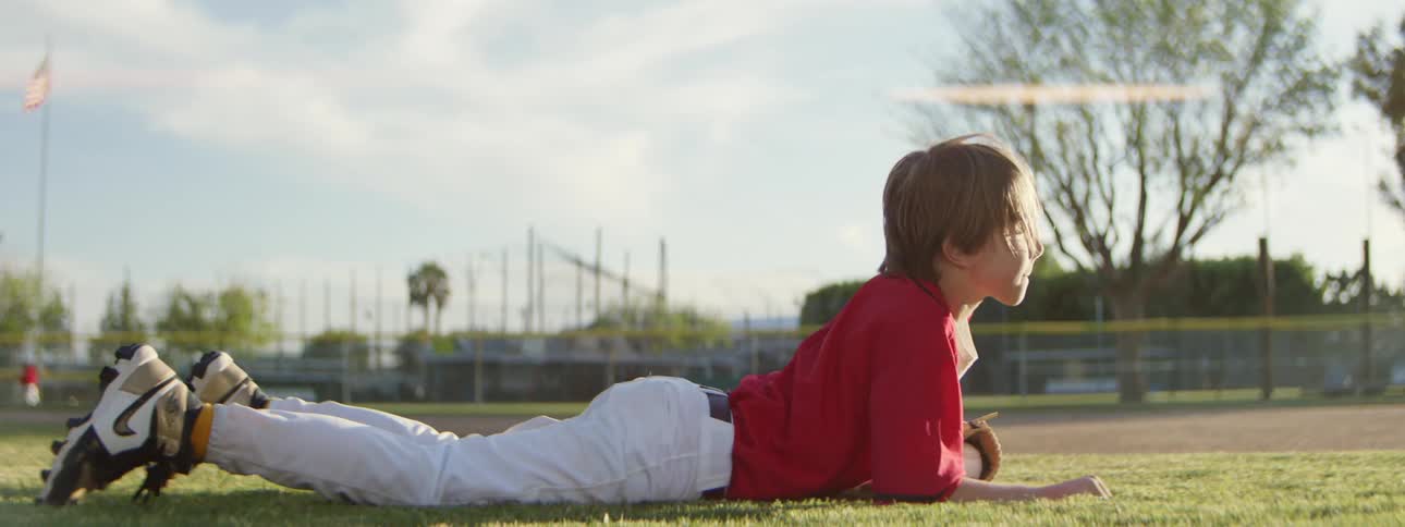 A young baseball player makes an incredible diving catch on a sunny field in slow motion