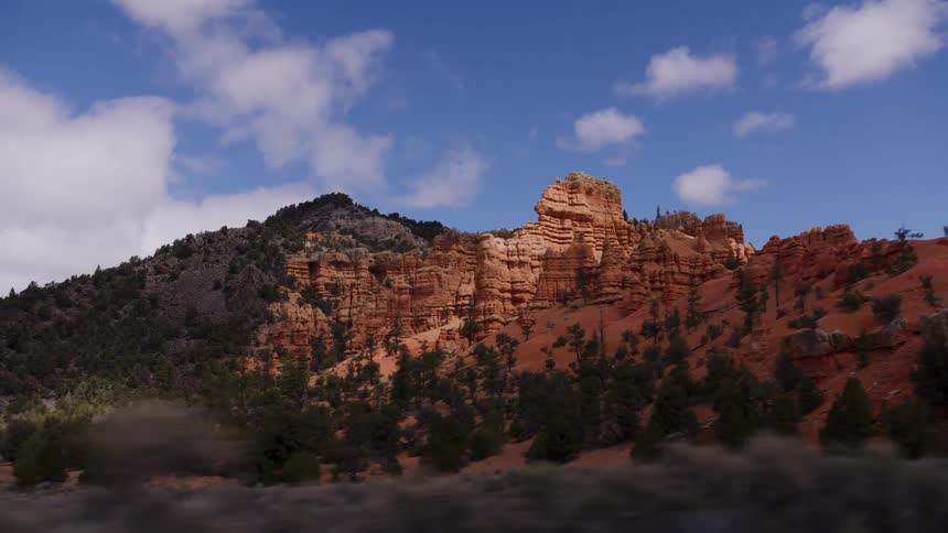 A slow-motion, drive-by view of sunlit red rock formations in a stunning desert landscape