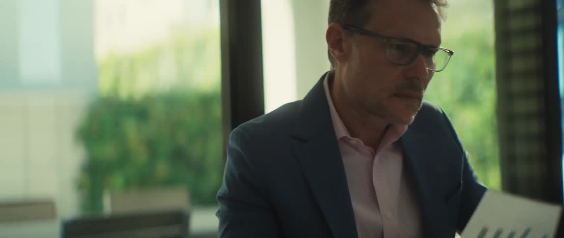 A focused businessman in a suit and glasses analyzes a financial report while working on his laptop in a modern office