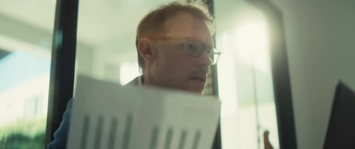 A serious businessman discusses a financial bar graph during a video conference in a sunlit office