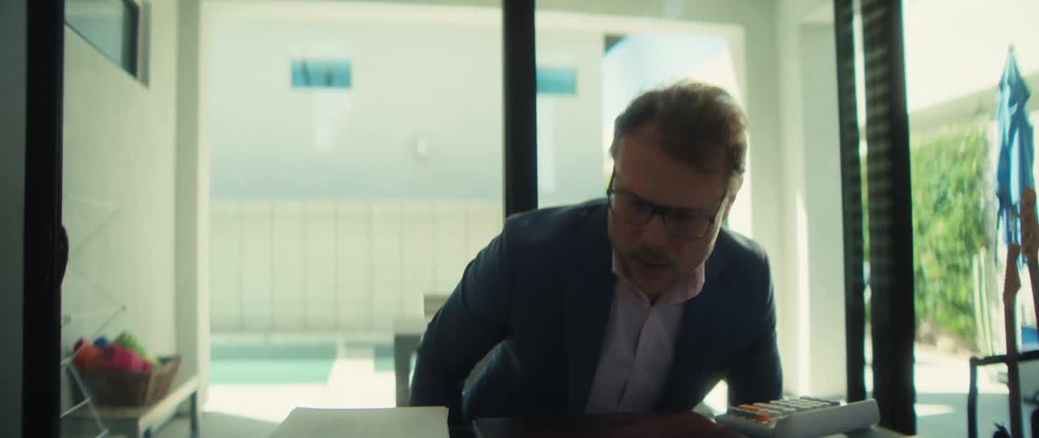 A serious businessman sits down at his modern desk, opens his laptop, and begins his workday
