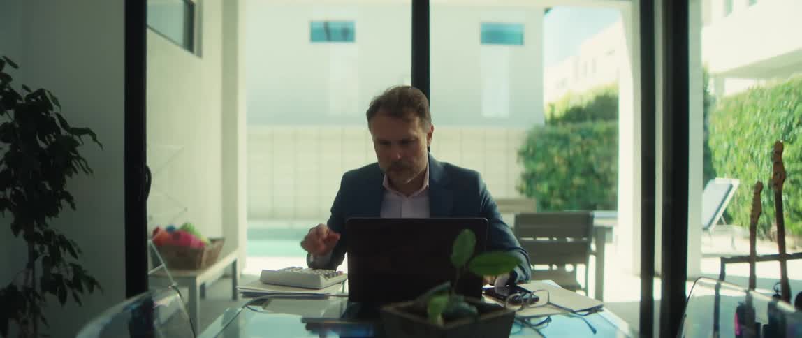 A successful businessman working from home at his dining room table celebrates good news he sees on his laptop