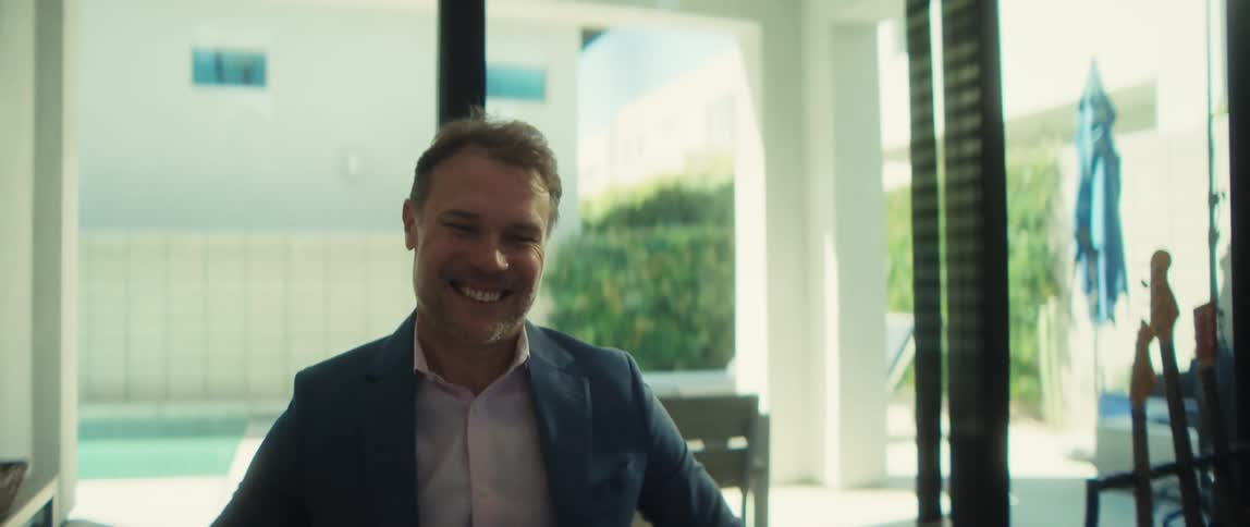 A professional man in a suit working from home looks up from his screen and breaks into a joyous smile and claps his hands
