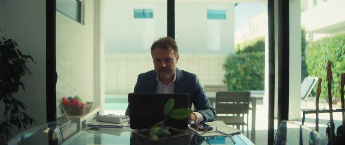 A focused businessman working from his home office calculates figures, then looks at his laptop and smiles with satisfaction