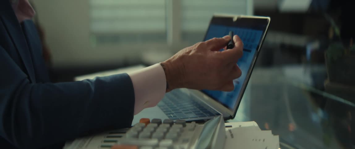 A serious financial professional works at his desk, analyzing data on a laptop and using a calculator