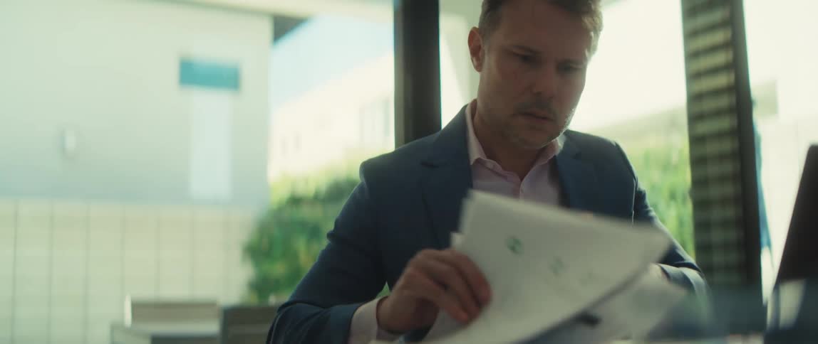 A serious businessman works on his laptop and carefully reviews a stack of papers with graphs in slow motion