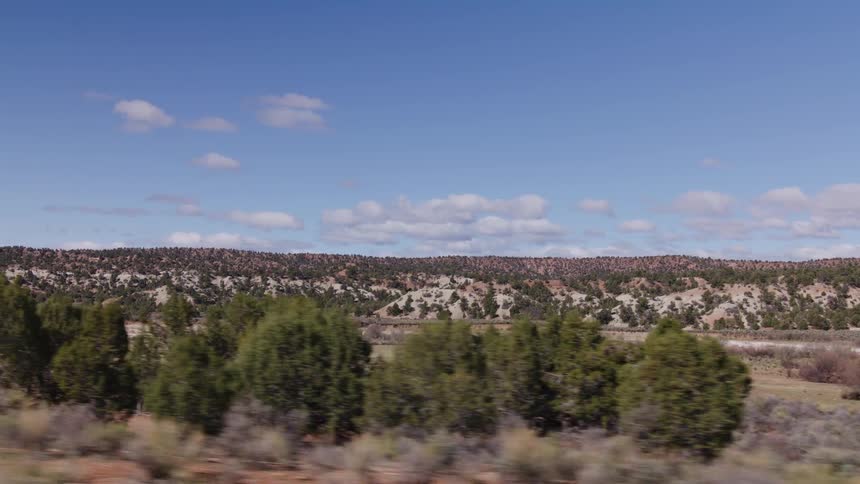 A smooth tracking shot reveals the rugged beauty of a high desert landscape with tree-covered hills under a brilliant blue sky