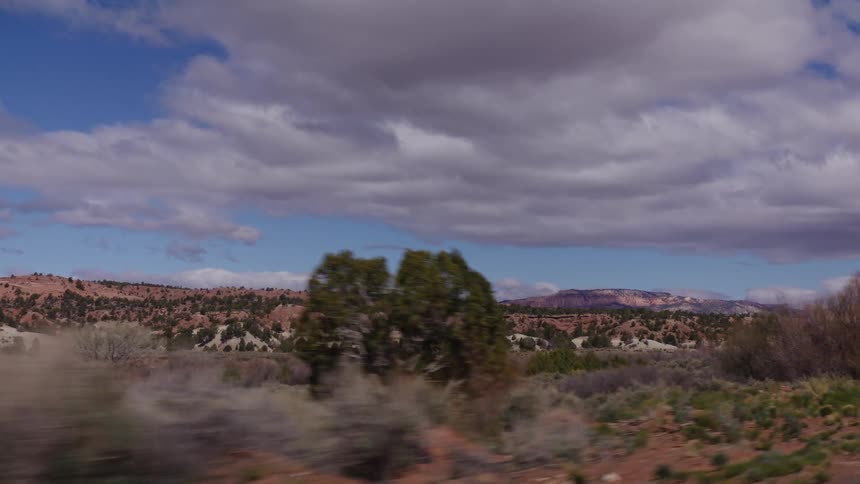 A slow dolly shot travels through the desert landscape of Southern Utah, with red rock hills and a vast, cloudy sky