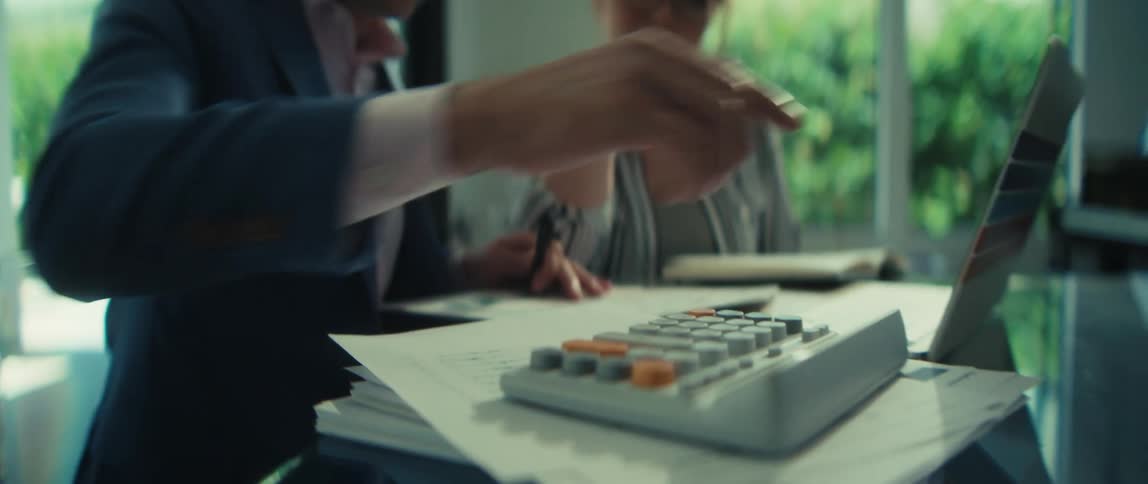 A businessman and a businesswoman analyze financial documents and use a calculator during a professional meeting in a modern office
