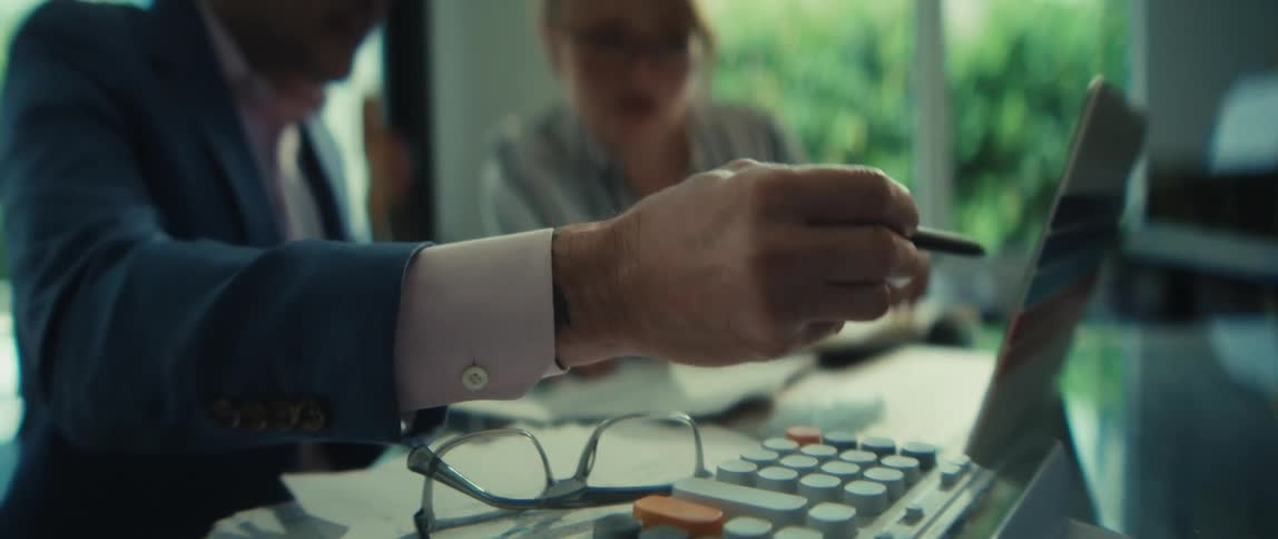 A professional man and woman collaborate in a modern office, seriously discussing and analyzing financial charts on a laptop