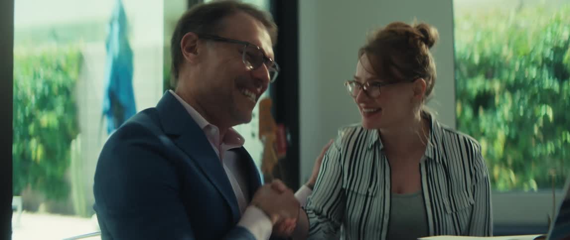 Two business colleagues laugh and shake hands after a successful meeting in a modern office