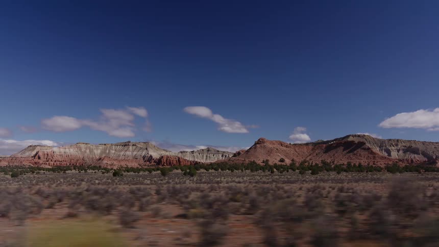 Driving past the stunning multi-colored buttes and mesas of a vast desert landscape under a clear blue sky