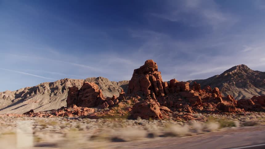 Driving alongside striking red rock formations in a sunny desert landscape with a truck in the foreground
