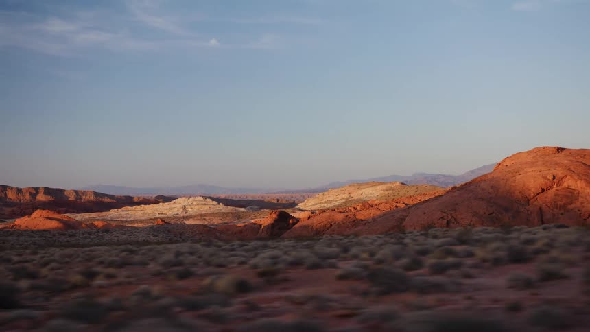 A beautiful tracking shot from a moving car shows the stunning red rock formations of a desert landscape illuminated by the golden hour sun