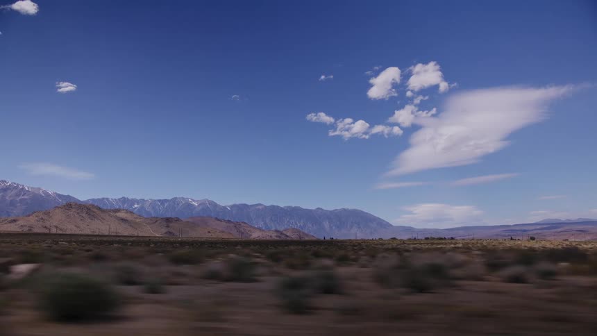 A scenic drive through a vast desert landscape with snow-capped mountains under a clear blue sky