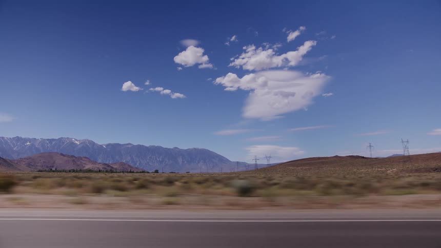 A scenic drive along a desert highway with snow-capped mountains in the distance under a vast blue sky
