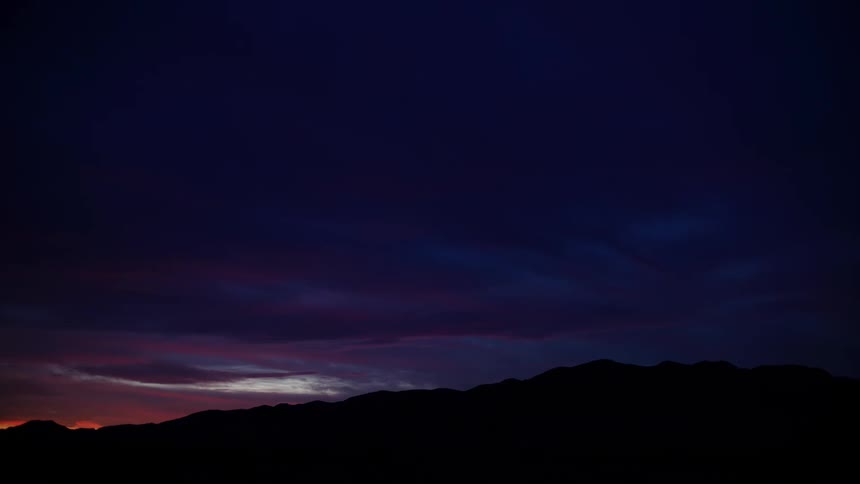 The last glimmer of sunset glows beneath a deep purple and blue sky over a mountain silhouette