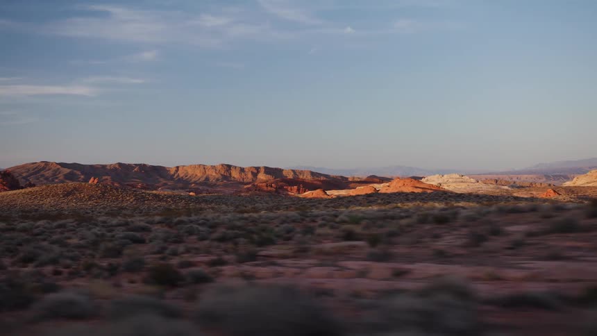 A scenic drive through a vast desert landscape with red rock formations during a beautiful golden hour sunset