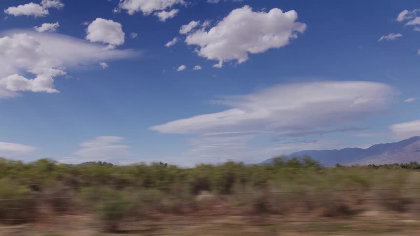 View from a moving vehicle looking out at a vast desert landscape with mountains in the distance under a blue sky