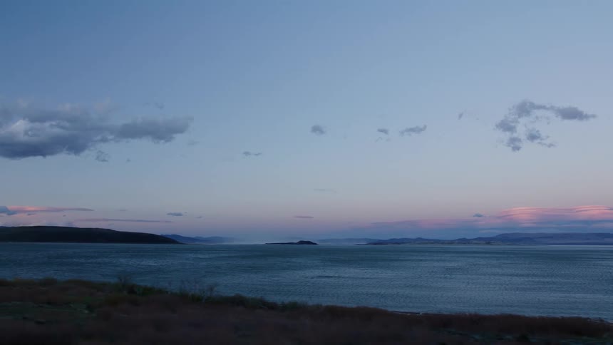 A tranquil drive along a scenic highway next to a vast lake at dusk, with pastel colors painting the sky