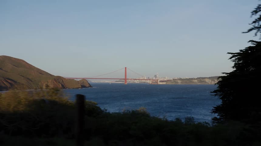 A scenic tracking shot reveals the iconic Golden Gate Bridge and San Francisco skyline across the bay from a forested viewpoint
