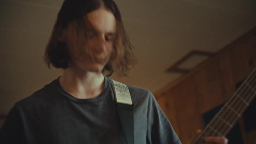 Teenage bass player with long hair gets into the groove while rehearsing with his band in a home studio