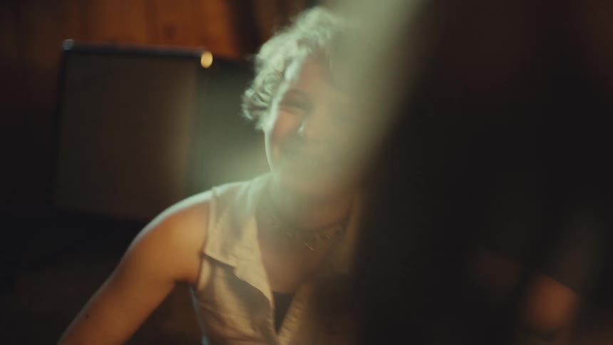 An energetic teenage girl with curly hair and braces laughs and dances with excitement while talking to a friend