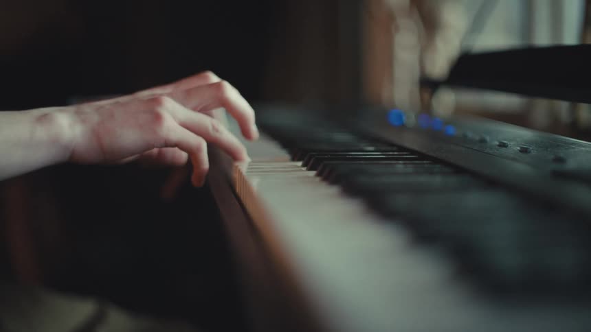 An intimate, artistic close-up shot of a person's hands gracefully playing a melody on an electric piano