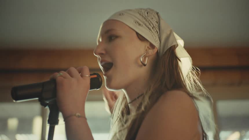 A passionate female vocalist in a bandana sings into a microphone during a band practice in slow motion