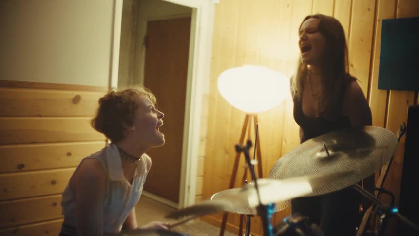 A female singer and drummer passionately sing together during an energetic band rehearsal in a music studio