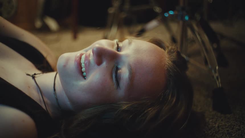 A young woman lies on the floor of a music studio, a blissful smile appearing on her face as she listens