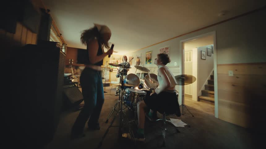 A young and energetic rock band practices their music in a home studio, with the singer dancing and the drummer playing intensely