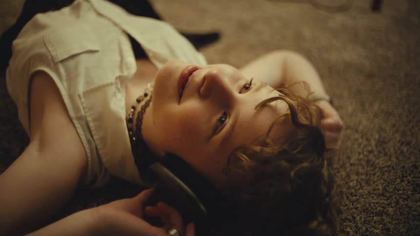Upward-looking shot of a young person with braces relaxing on the floor and smiling while listening to headphones