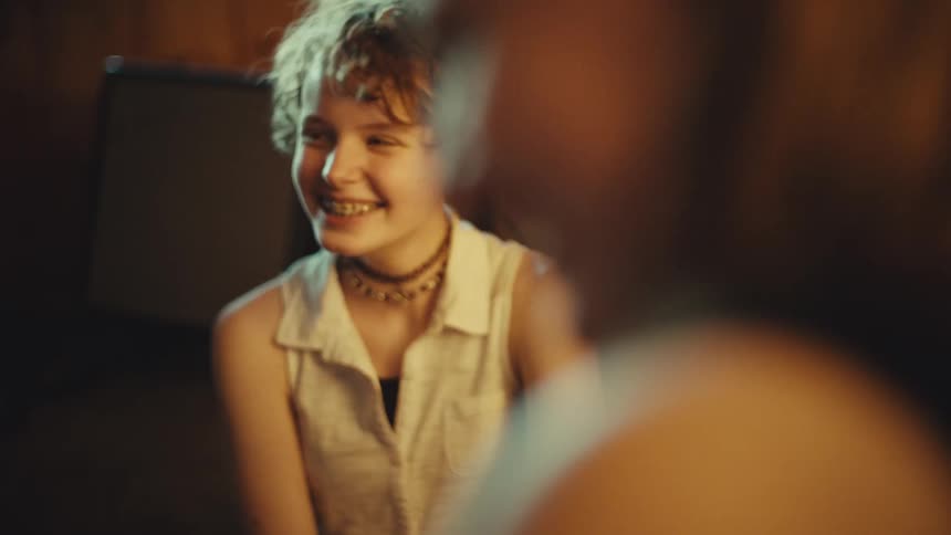 A happy teenager with curly hair and braces laughs wholeheartedly while having a fun conversation with a friend in slow motion