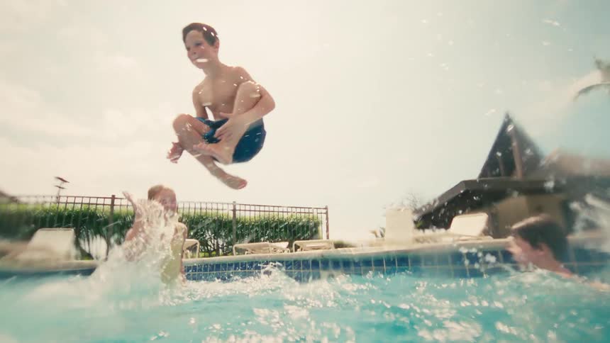 A young boy jumps into a swimming pool in a cannonball, captured in slow motion from an underwater perspective