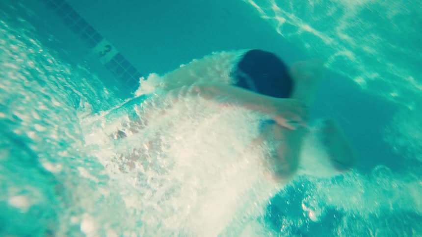 An exciting underwater shot captures two kids jumping and splashing into a bright blue swimming pool on a sunny day