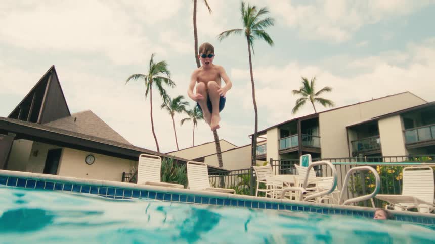 Slow motion underwater view of a young boy with goggles jumping into a swimming pool at a tropical resort