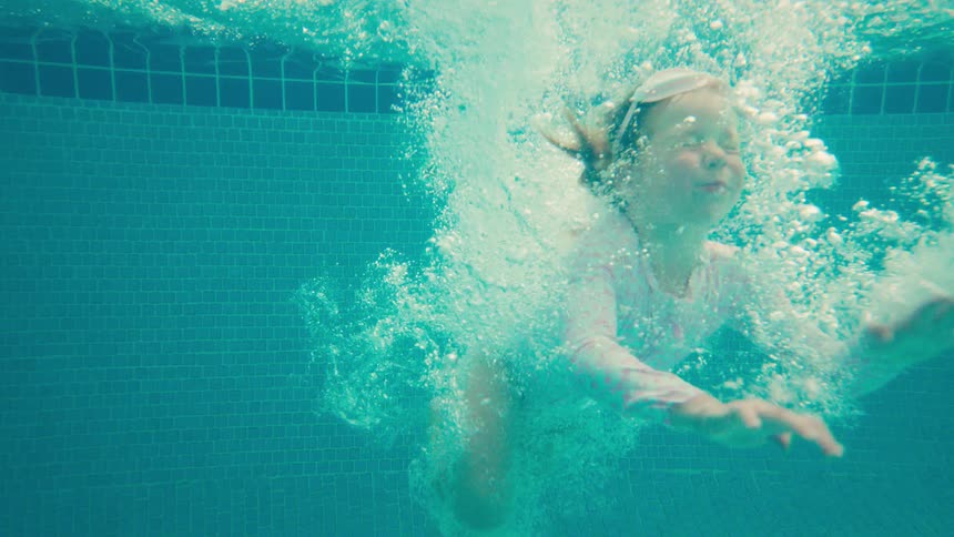 A happy young girl jumps into a tropical swimming pool in slow motion, captured with an exciting underwater splash