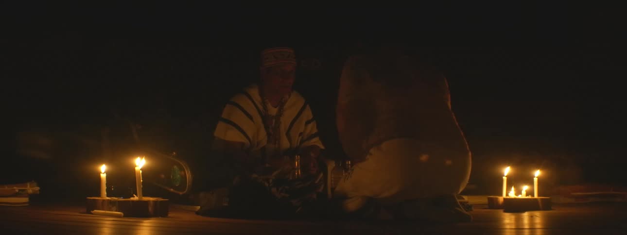 An indigenous shaman in traditional attire conducts a sacred healing ritual by candlelight at night