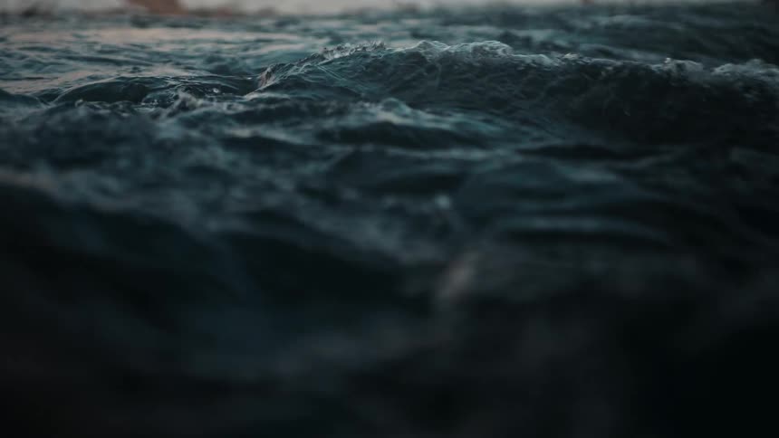 Turbulent dark blue water churns and flows in a dramatic slow-motion close-up